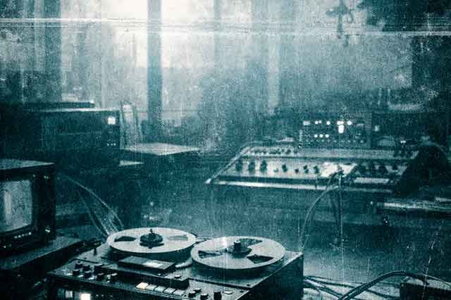 Habitación pequeña con sintetizadores y cables en tonos fríos, evocando la estética industrial y experimental de Esplendor Geométrico en Madrid 1982