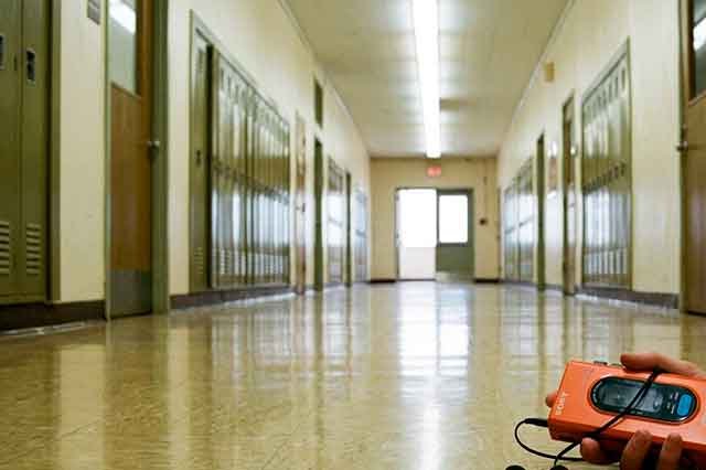Pasillo vacío de un instituto de los 80 con luz fría y un walkman en primer plano, evocando la distancia emocional de “Tan Lejos”.